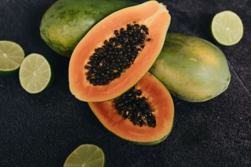 Fresh sliced papayas with black seeds alongside limes on a dark surface highlighting papaya benefits for gut health