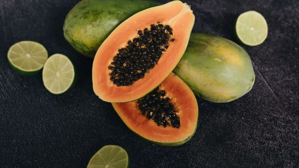 Fresh sliced papayas with black seeds alongside limes on a dark surface highlighting papaya benefits for gut health