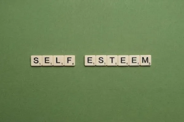 Scrabble letter tiles spelling 'SELF ESTEEM' arranged on a green textured background, symbolizing confidence and personal growth.